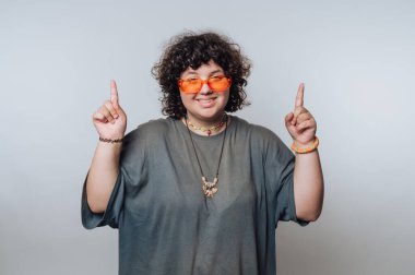 Kıvırcık saçlı, turuncu güneş gözlüğü takan biri, sıradan bir toplantı sırasında parlak bir iç mekanda neşeli jestler yapar.