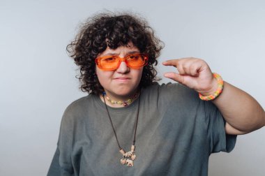 Kıvırcık saçlı ve güneş gözlüklü genç adam parlak bir mekanda küçük bir jest yapıyor.