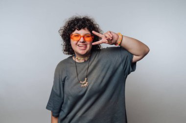 Kıvırcık saçlı, şık turuncu gözlüklü barış işareti ve kapalı mekan ortamında neşeli ifadeli biri.
