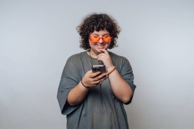 Turuncu gözlüklü genç, kapalı alanda akıllı telefon kullanırken gülümsüyor.