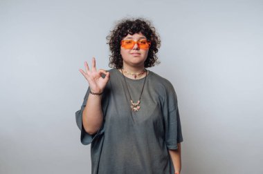 Gündelik kıyafetli genç adam modern bir iç mekanda el hareketi yapıyor.