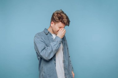 Hüsrana uğramış genç bir adam, sıradan bir ortamda mavi bir arkaplan karşısında dururken...