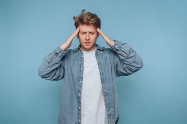 Stresli bir anda mavi bir arka plana kafasını yaslamış genç bir adam.