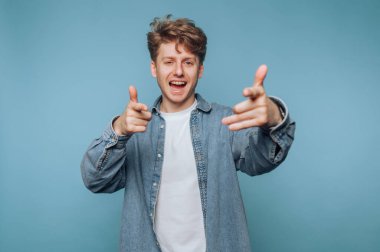 Genç adam gülümsüyor ve el hareketleriyle oynuyor. Parlak mavi bir arka plana karşı. Sıradan bir ortamda.