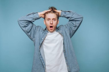 Şaşırmış genç adam, elleri başının üstünde, mavi bir zemine çarpıyor.