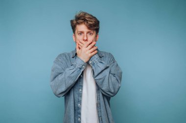 Açık mavi arka planda elleri olan genç bir adam sürpriz ya da şok etkisi yaratıyor.