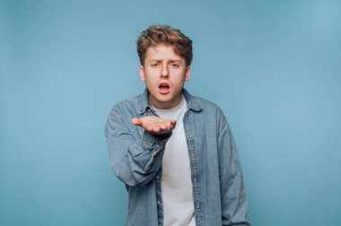 İç mekan ortamında mavi arka plan önünde el hareketleriyle sürpriz yapan genç bir adam.