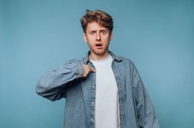 Şok olmuş bir ifadeyle şaşıran genç bir adam mavi arka planda sıradan bir kıyafet giyiyor.