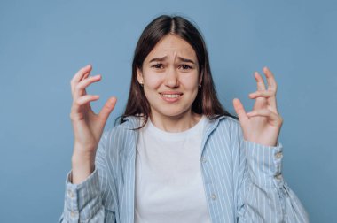 Mavi bir ortamda hayal kırıklığını ifade eden genç bir kadın. Elleri öfke ve yüz duygusuyla havada.