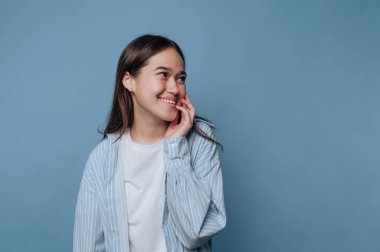 Gülümseyen ve mavi bir arkaplanda poz veren genç bir kadın.