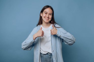 Genç bir kadın mavi arka planda başparmağıyla sevinçten havalara uçuyor.