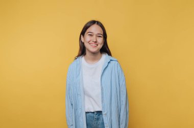 Çizgili tişört giymiş gülümseyen genç bir kadın neşeli bir atmosferde parlak sarı bir arka planda duruyor.