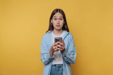 Sarı arkaplan önünde akıllı telefon tutan genç bir kadın.