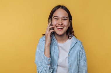 Gülümseyen genç bir kadın telefonda canlı sarı bir arka planda konuşuyor.