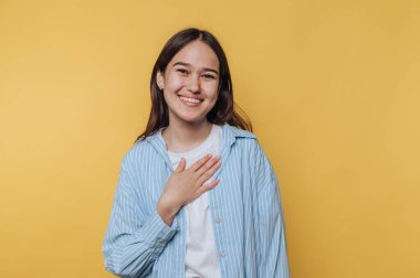 Gündelik giysiler içinde gülümseyen genç bir kadın canlı sarı bir arka plana karşı sıcak bir karşılama sunar.