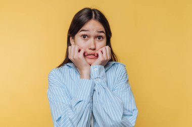 Genç kadın korku ve şaşkınlığını kapalı bir alanda parlak sarı bir arkaplan karşısında ifade ediyor.