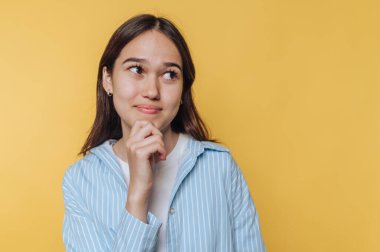 Düşünceli bir ifadeyle düşünen genç bir kadın. Sıradan bir kıyafetin içinde parlak sarı bir arka plana karşı.
