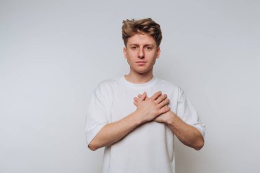 Gün ışığında sakin bir ortamda elleri göğsünde duygularını ifade eden genç bir adam.