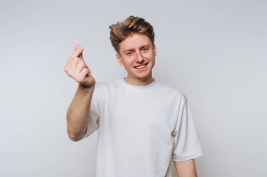 Genç adam gülümsüyor ve sıradan bir ortamda tarafsız bir arkaplana el hareketi yapıyor.