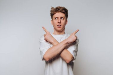 Erkek, minimalist bir stüdyo ortamında çapraz kollar ve karışık bir ifadeyle kafa karıştırıcı bir şekilde hareket eder.