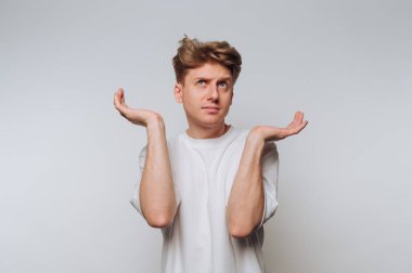 Adam, nötr bir stüdyoda gündüz saatlerinde ellerini kaldırarak kafa karışıklığını ifade ediyor.