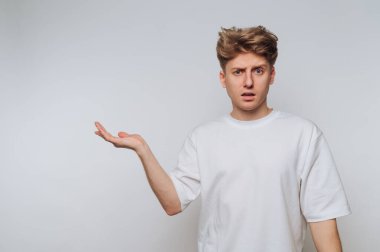 Gündüz saatlerinde minimalist bir stüdyoda el kaldırarak kafa karışıklığını ifade eden genç adam.