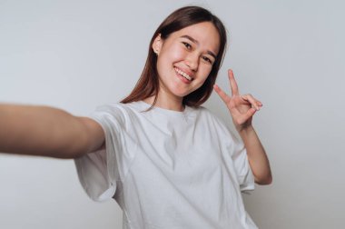 Genç bir kadın gülümser ve sade beyaz gömlekli bir selfie için poz verir.