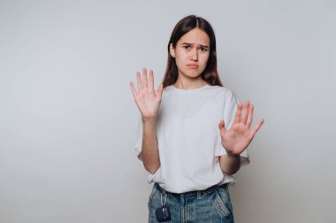 Tarafsız bir arkaplanda ellerini kaldırarak endişe ve tereddütlerini dile getiren genç bir kadın.