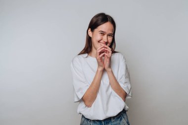 Neşeli bir gülümsemeyle neşe saçan genç bir kadın tarafsız bir arkaplanda dikiliyor.