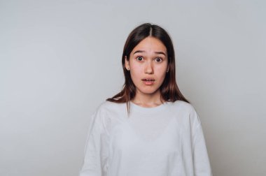 Tarafsız bir arkaplanda beyaz bir gömlek giyerken şaşırdığını ifade eden genç bir kadın.