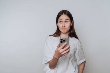 Kapalı alandaki minimalist bir mekanda akıllı telefon tutan genç bir kadın.