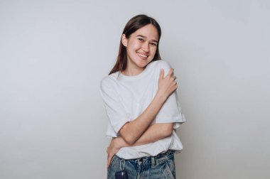 Tarafsız bir arkaplanda rahat bir şekilde gülümseyen genç bir kadın.