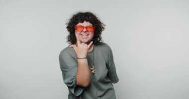 Gülümseyen genç kadın gururla neşeli bir el işareti sergiliyor, kendine güven ve mutluluk yayıyor, beyaz arka planda neşeli kendini ifade etmenin özünü yakalıyor.