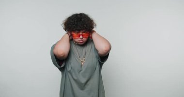 Kıvırcık saçlı ve kırmızı gözlüklü genç kıvırcık kadın beyaz arka planda şaşırtıcı duygular sergiliyor.