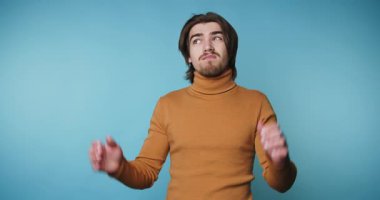 Balıkçı yakalı genç adam, mavi arka planda kafa karışıklığı yaratarak, omuz silkerek inançsızlığı tasvir ediyor.