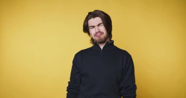 Genç adam sarı arka planda gözüne dokunurken dalgın görünüyor.