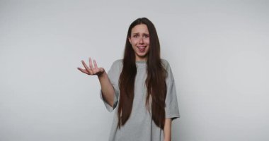 Kafası karışmış kadın, sıradan gri gömleğiyle sade arka planda şaşkınlık yaşıyor.