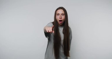 Şok olmuş bir kadın beyaz arka planda kamerayı işaret ediyor. Kadın minimalist ortama olan şaşkınlığını ve şaşkınlığını ifade ederken yakalanan sürpriz an