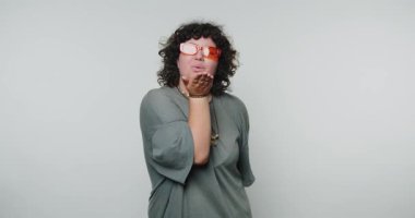 Şık gözlüklü genç bir kadın minimalist stüdyo ortamında bir öpücük yolluyor.