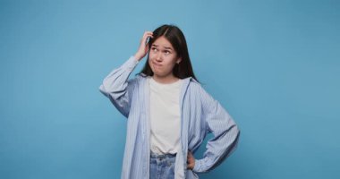 Kafasını mavi bir arka plana sürterken kafasının karıştığını gösteren bir kız.