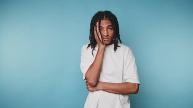 Mavi arka planda yorgun Afro-Amerikan bir adam. Uykulu yüzüyle kameraya bakıyor..