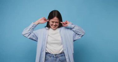 Bir stüdyo seansı sırasında canlı mavi arka planlı yüksek sese tepki olarak kadın kulaklarını kapatır.