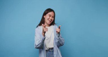 Gülümseyen genç bir kadın mavi bir arkaplanda şevk ve güven göstererek şakacı bir poz veriyor.