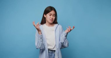 Kafası karışmış kız duygularını ifade ederken mavi arka planda duruyor.