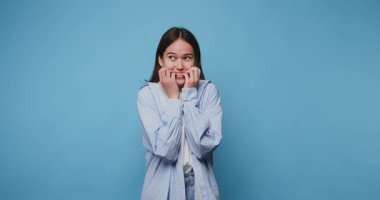 Çekici Asyalı kız mavi arka planda korkmuş yüzüyle gergin. Genç bir kadın, neşeli bir stüdyo ortamında heyecanı ifade ediyor. Mavi arka planı da gün ortası civarında.