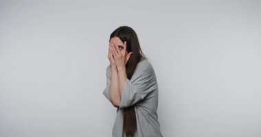 Kapalı mekan ortamında gülümseyen genç bir kadın şakacı bir şekilde yüzünü gizliyor.