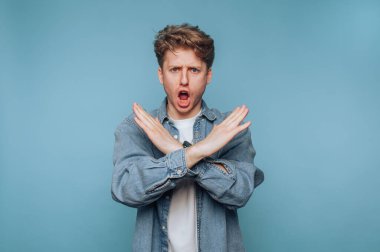 Kot ceket ve beyaz gömlek giyen genç bir adam, önünde kollarını kavuştururken güçlü bir ifade sergiliyor..