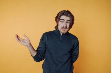 Orta boylu, kahverengi saçlı, düşünceli, canlı sarı bir fonda duran genç bir adam. Siyah bir kazak giyiyor ve sohbet ediyor gibi görünüyor..