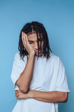 Saçları örgülü genç bir çocuk alnını eline dayayarak hayal kırıklığını gösterir. Pürüzsüz mavi bir zemin üzerinde duruyor, kollarını kavuşturup, bir rahatsızlık hissi veriyor..