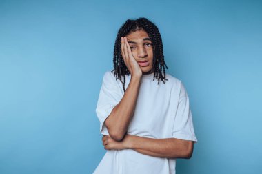 Genç bir birey parlak mavi bir arka plana karşı duruyor, dalgın dalgın bakarken ellerini yüzlerine koyuyor. Rahat pozları düşünceli ya da hayalperest bir hava veriyor..